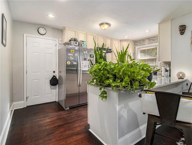 kitchen with stainless steel refrigerator, kitchen peninsula, dark hardwood / wood-style flooring, and light stone countertops