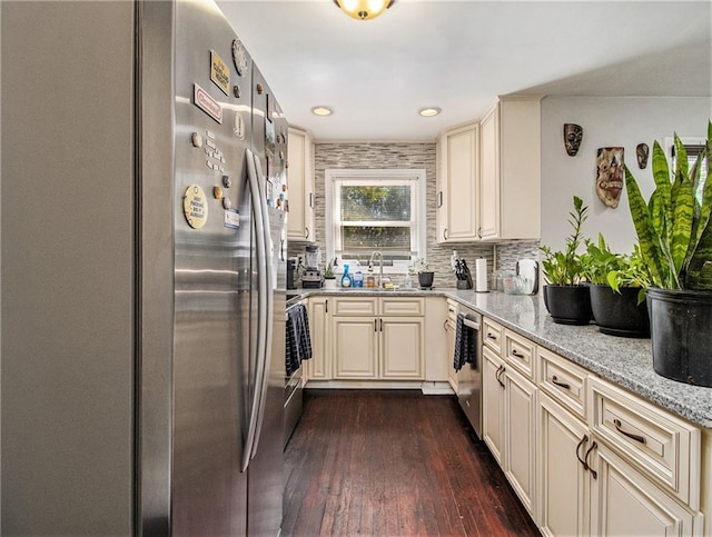 kitchen with light stone counters, stainless steel appliances, cream cabinetry, and dark hardwood / wood-style flooring