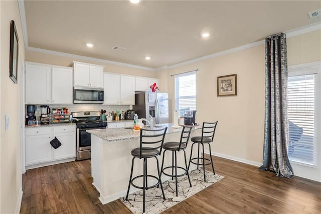 kitchen featuring a kitchen bar, a kitchen island with sink, light stone countertops, stainless steel appliances, and white cabinets