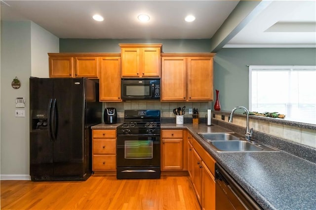 kitchen with black appliances, a sink, light wood finished floors, tasteful backsplash, and dark countertops