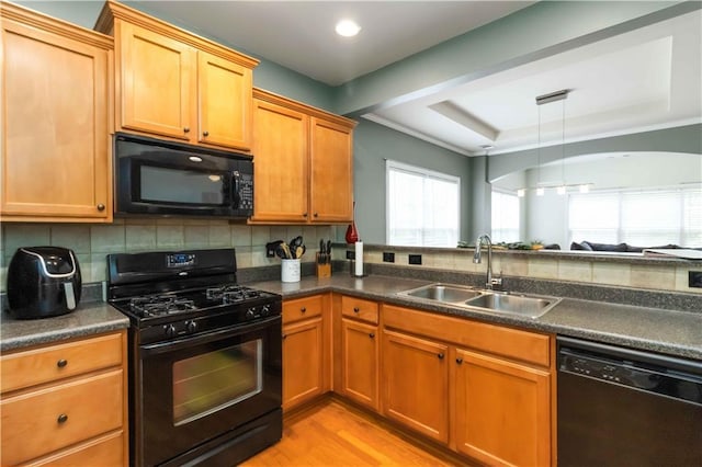 kitchen featuring black appliances, a sink, dark countertops, a tray ceiling, and light wood-style floors