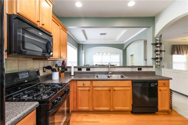 kitchen featuring black appliances, a sink, a raised ceiling, light wood finished floors, and recessed lighting