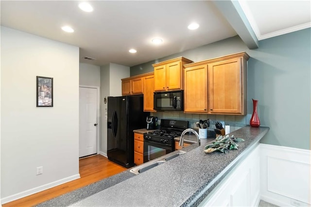 kitchen featuring black appliances, light wood-style floors, recessed lighting, a sink, and a wainscoted wall