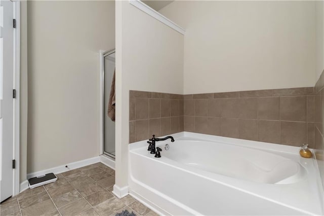 bathroom featuring a stall shower, a bath, and baseboards