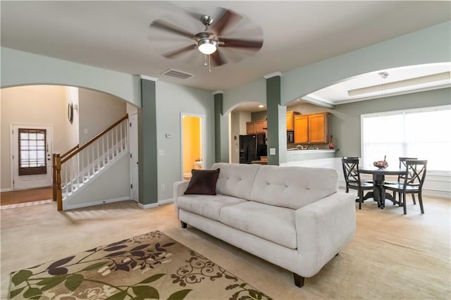 living room with arched walkways, light colored carpet, and ceiling fan