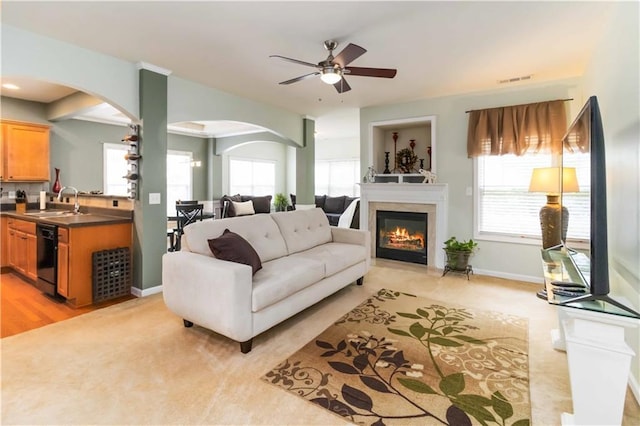 living room with arched walkways, light colored carpet, ceiling fan, a glass covered fireplace, and baseboards
