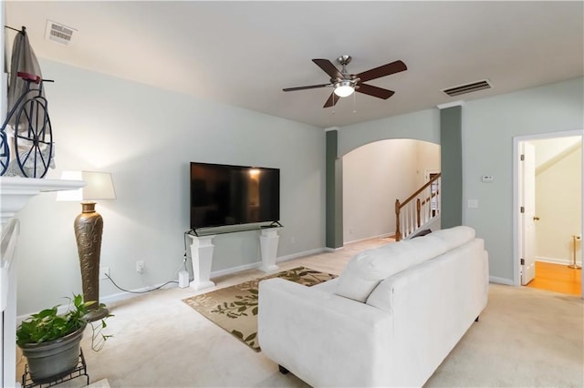 living area featuring arched walkways, light carpet, ceiling fan, and stairs