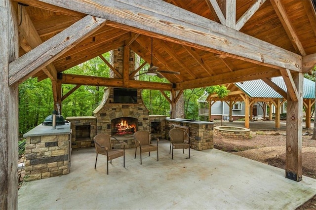 view of patio / terrace with a gazebo, ceiling fan, an outdoor kitchen, and an outdoor stone fireplace