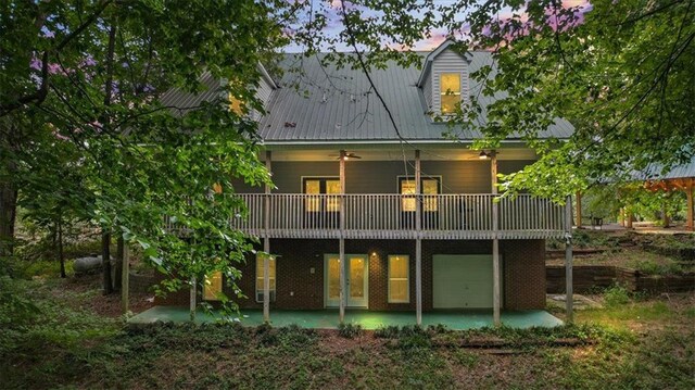 back house at dusk featuring a wooden deck, a garage, and a patio