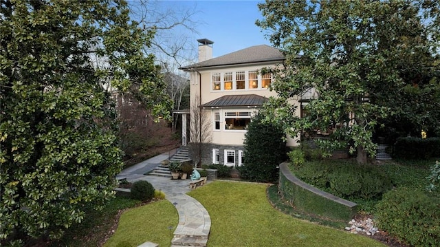 back of property featuring a yard, a chimney, stucco siding, a standing seam roof, and metal roof