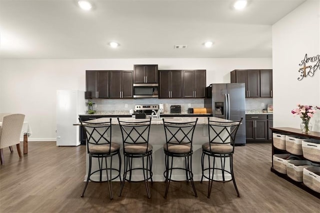 kitchen featuring appliances with stainless steel finishes, visible vents, dark brown cabinetry, and a kitchen breakfast bar