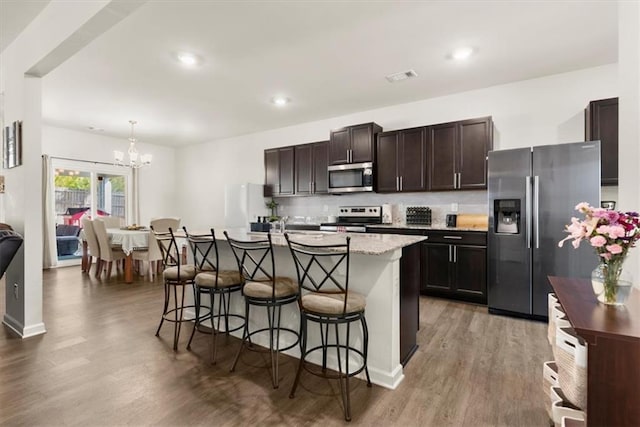 kitchen featuring dark brown cabinetry, visible vents, a breakfast bar, wood finished floors, and stainless steel appliances