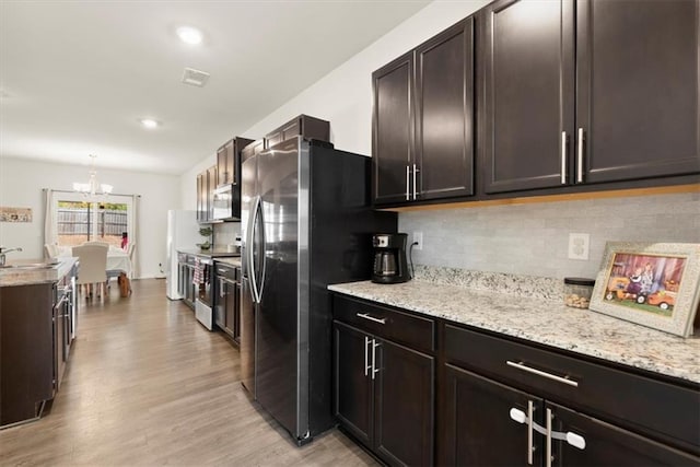 kitchen featuring stainless steel appliances, visible vents, light wood-style floors, decorative backsplash, and light stone countertops