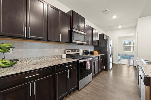 kitchen featuring tasteful backsplash, visible vents, wood finished floors, light stone countertops, and stainless steel appliances