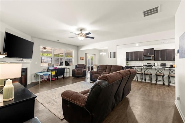 living area featuring ceiling fan with notable chandelier, a glass covered fireplace, wood finished floors, and visible vents