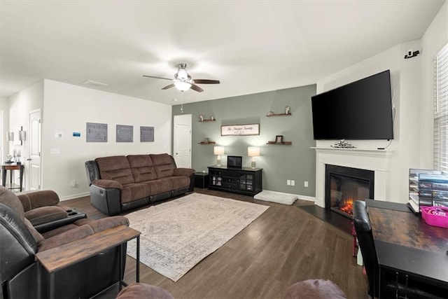 living room with a ceiling fan, a glass covered fireplace, baseboards, and wood finished floors