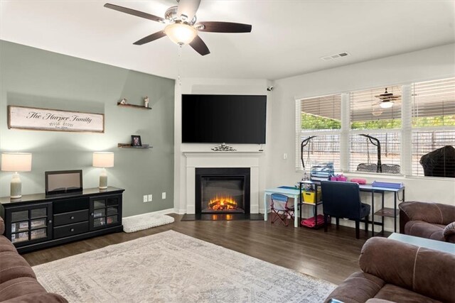 living area featuring visible vents, baseboards, a glass covered fireplace, ceiling fan, and wood finished floors