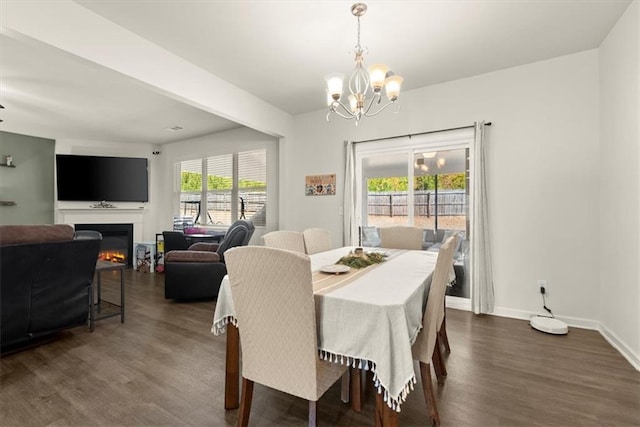 dining space featuring dark wood-type flooring, a lit fireplace, baseboards, and an inviting chandelier