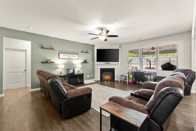 living area featuring ceiling fan, a glass covered fireplace, wood finished floors, and baseboards