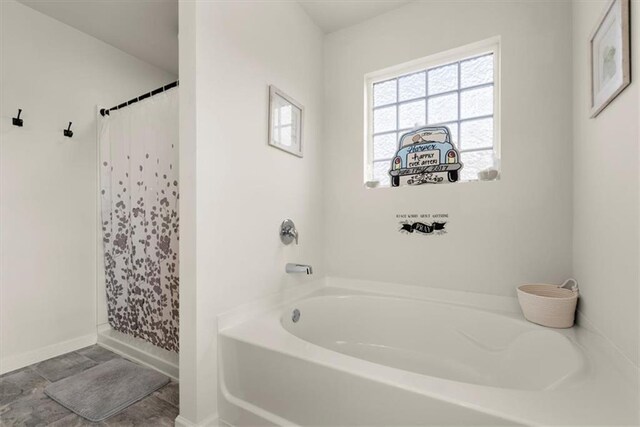 bathroom featuring a shower with shower curtain, baseboards, and a bath