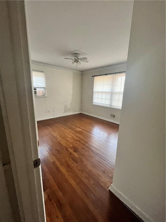 unfurnished room with a ceiling fan, dark wood finished floors, baseboards, and ornamental molding