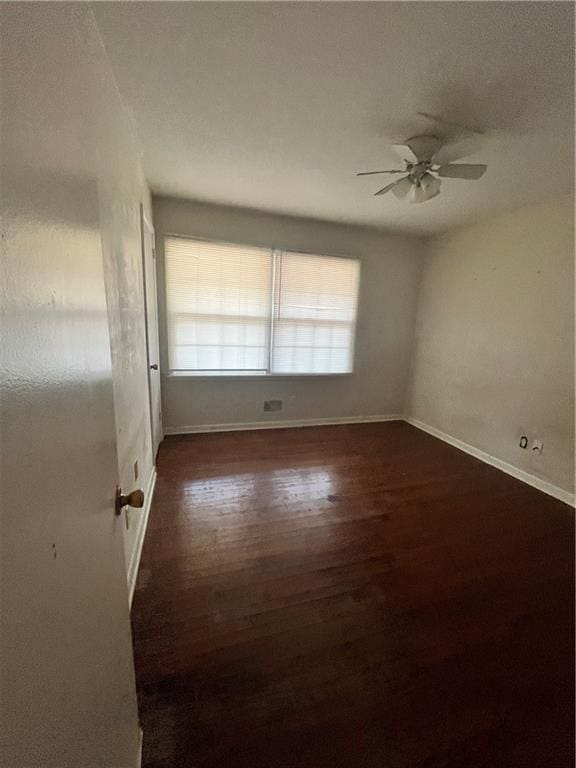 empty room with dark wood finished floors, a ceiling fan, and baseboards