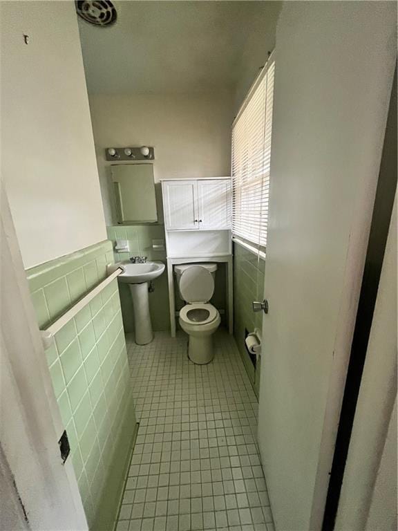 bathroom with toilet, wainscoting, tile patterned flooring, and tile walls