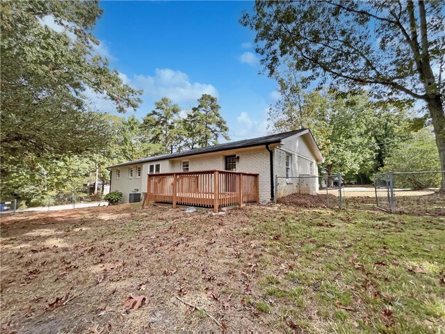 rear view of property featuring central AC unit, a yard, and a wooden deck