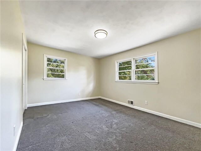 unfurnished room with plenty of natural light and dark carpet