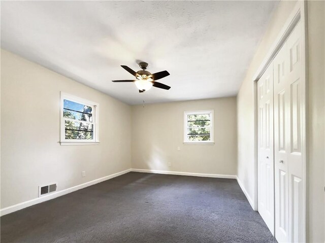 unfurnished bedroom featuring dark colored carpet, multiple windows, ceiling fan, and a closet