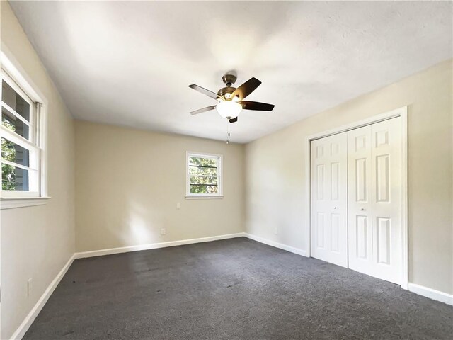 unfurnished bedroom with dark colored carpet, ceiling fan, and a closet