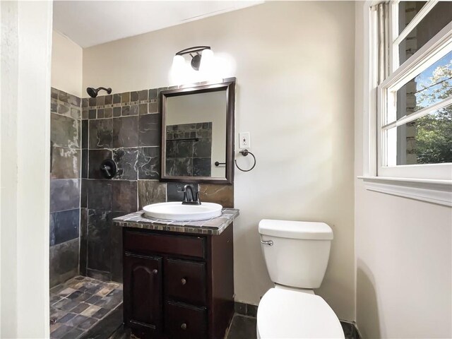 bathroom with a tile shower, vanity, and toilet