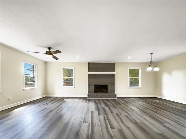 unfurnished living room with a fireplace, ceiling fan with notable chandelier, a healthy amount of sunlight, and dark hardwood / wood-style floors