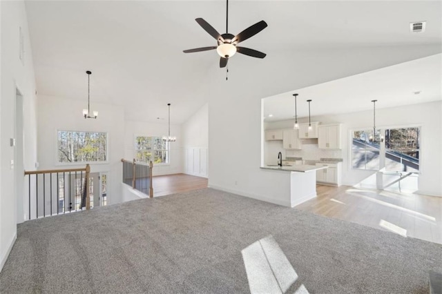 unfurnished living room with visible vents, light colored carpet, a sink, high vaulted ceiling, and ceiling fan with notable chandelier