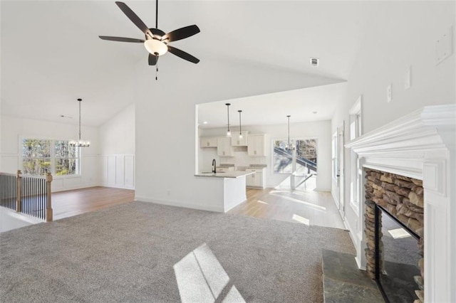 unfurnished living room with high vaulted ceiling, light colored carpet, plenty of natural light, and ceiling fan with notable chandelier