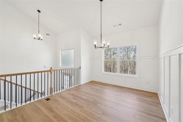 unfurnished dining area with a decorative wall, wood finished floors, a wainscoted wall, a chandelier, and vaulted ceiling