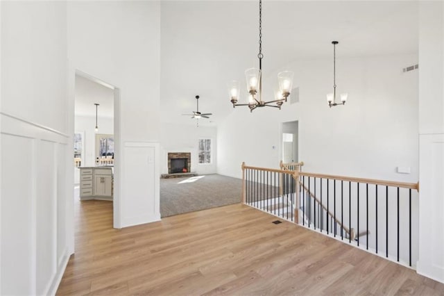 interior space with a chandelier, visible vents, high vaulted ceiling, an upstairs landing, and light wood-style flooring