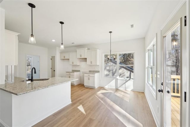 kitchen featuring a sink, light stone counters, light wood finished floors, and white cabinetry