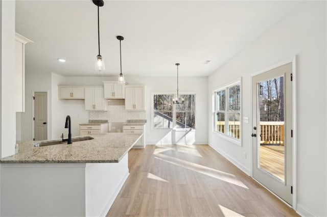 kitchen featuring light stone countertops, light wood-type flooring, white cabinets, tasteful backsplash, and a sink