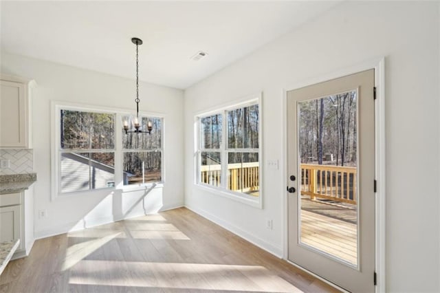 unfurnished dining area with visible vents, a chandelier, a healthy amount of sunlight, and light wood-style flooring