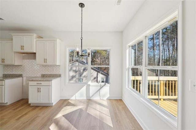 unfurnished dining area with baseboards, a chandelier, and light wood-style floors