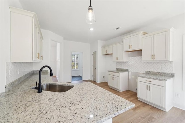 kitchen featuring decorative backsplash, a peninsula, light wood-type flooring, light stone counters, and a sink