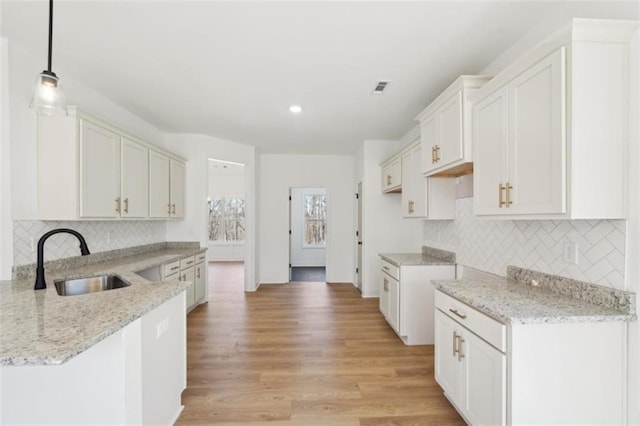 kitchen with light stone countertops, a sink, a peninsula, decorative backsplash, and visible vents