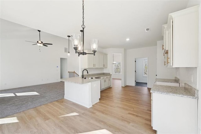 kitchen with light wood finished floors, ceiling fan with notable chandelier, a peninsula, and open floor plan