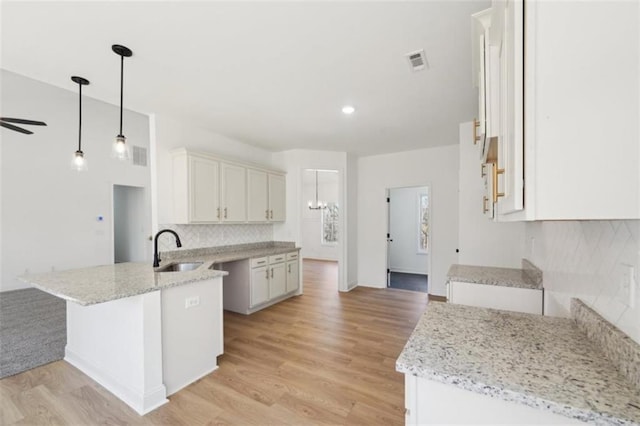 kitchen featuring light stone counters, a sink, a peninsula, tasteful backsplash, and visible vents