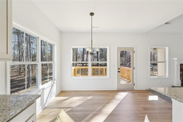 unfurnished dining area featuring visible vents, a notable chandelier, plenty of natural light, and light wood finished floors