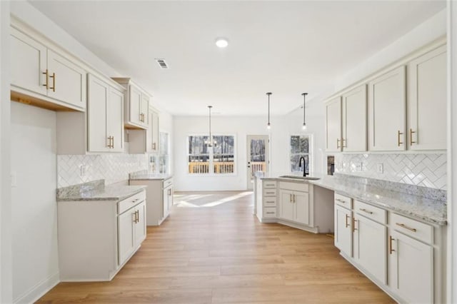 kitchen with light stone counters, a sink, light wood-style flooring, a peninsula, and tasteful backsplash