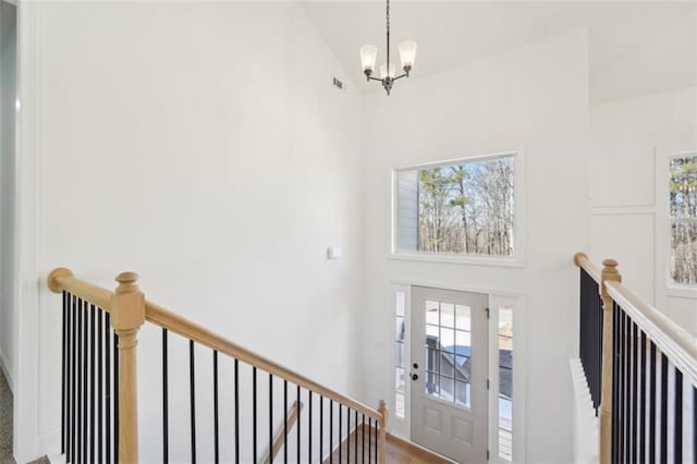 foyer featuring visible vents, a towering ceiling, a notable chandelier, and a wealth of natural light