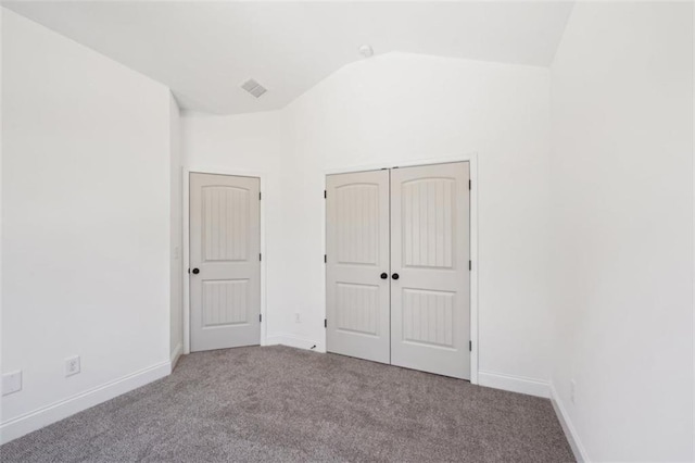 unfurnished bedroom with visible vents, a closet, lofted ceiling, baseboards, and carpet flooring