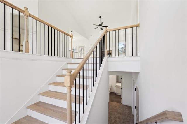 stairs with high vaulted ceiling and a ceiling fan